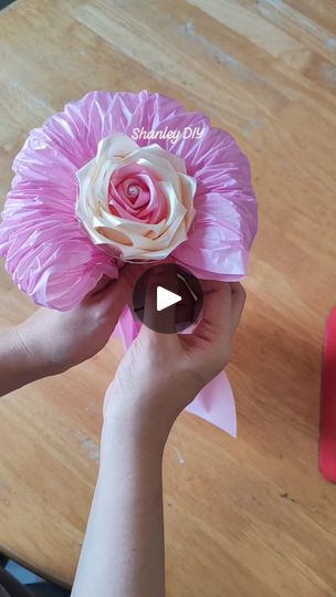 someone is holding a pink and white flower in front of a red box on a wooden table