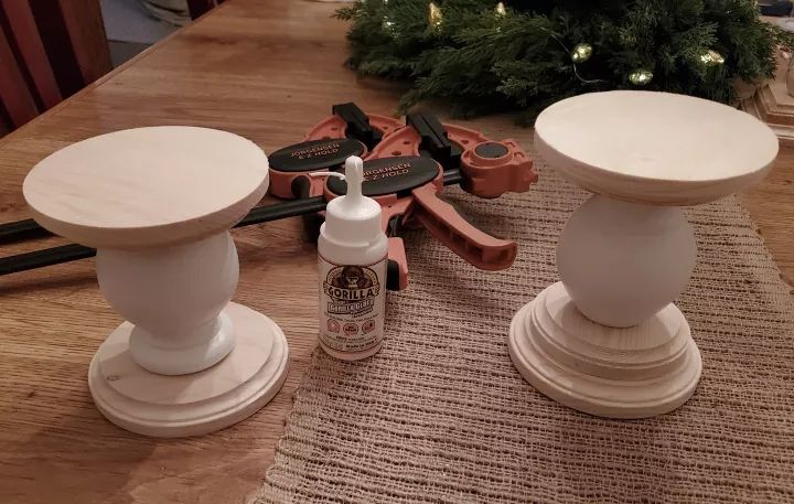 two white candlesticks sitting on top of a wooden table next to a christmas tree