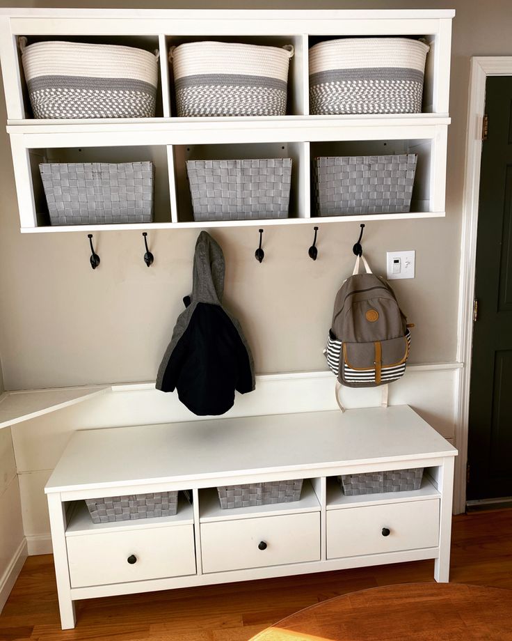 a white bench with baskets on it and two coats hanging from the wall behind it