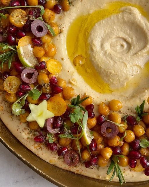 a platter with hummus, olives and cranberries on top of it