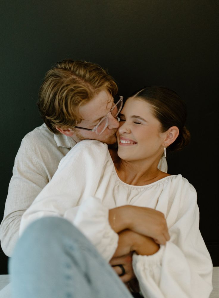 a man and woman sitting next to each other with their arms around each other while they are cuddling