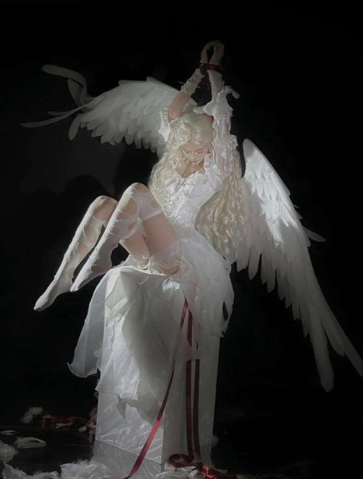 an angel statue sitting on top of a white cloth covered floor next to a red ribbon