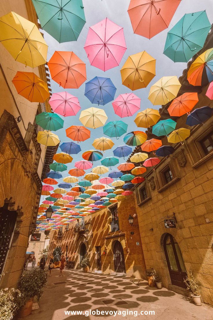 many colorful umbrellas are hanging from the ceiling in an alleyway with cobblestones