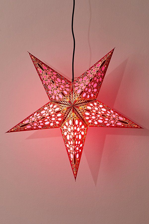 a red star shaped light hanging from a string on a pink wall next to a black cord