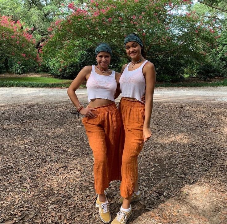 two young women standing next to each other in front of trees and dirt ground with their arms around each other