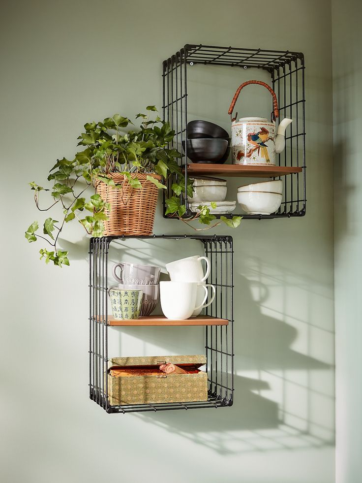 two metal shelves with plants and mugs on them in the corner of a room