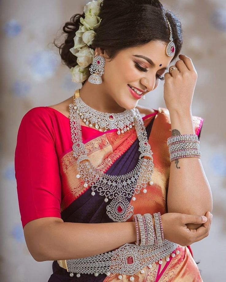 a woman in a sari is smiling and holding her hand to her ear while looking down