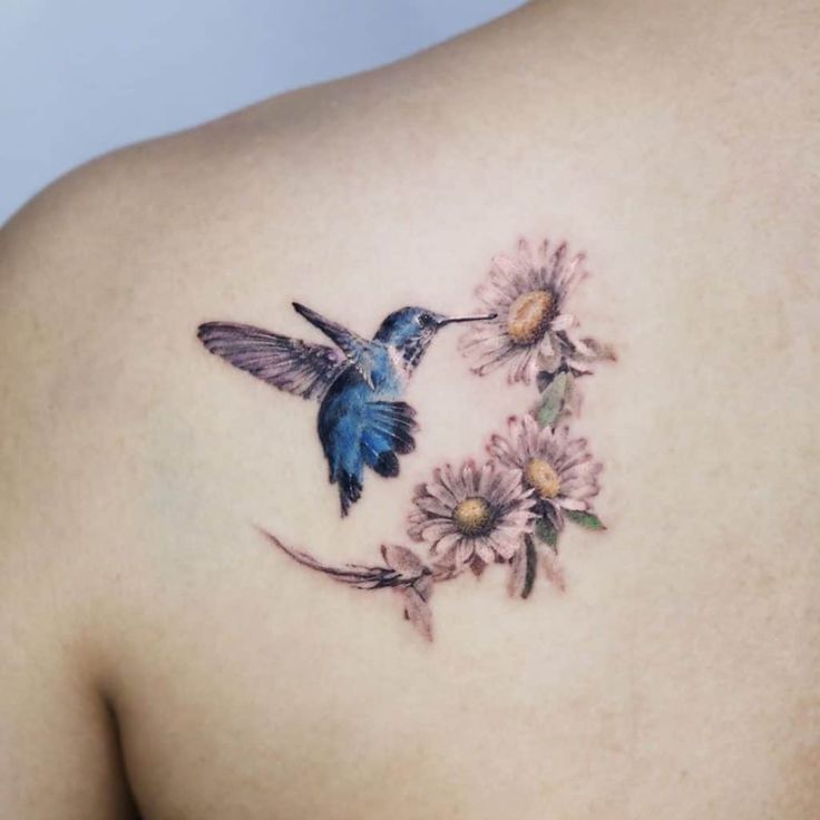 a small blue bird flying next to some pink flowers on the back of a woman's shoulder