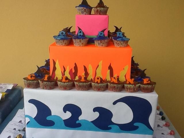 cupcakes are arranged on top of a cake with flames in the middle and blue waves around it