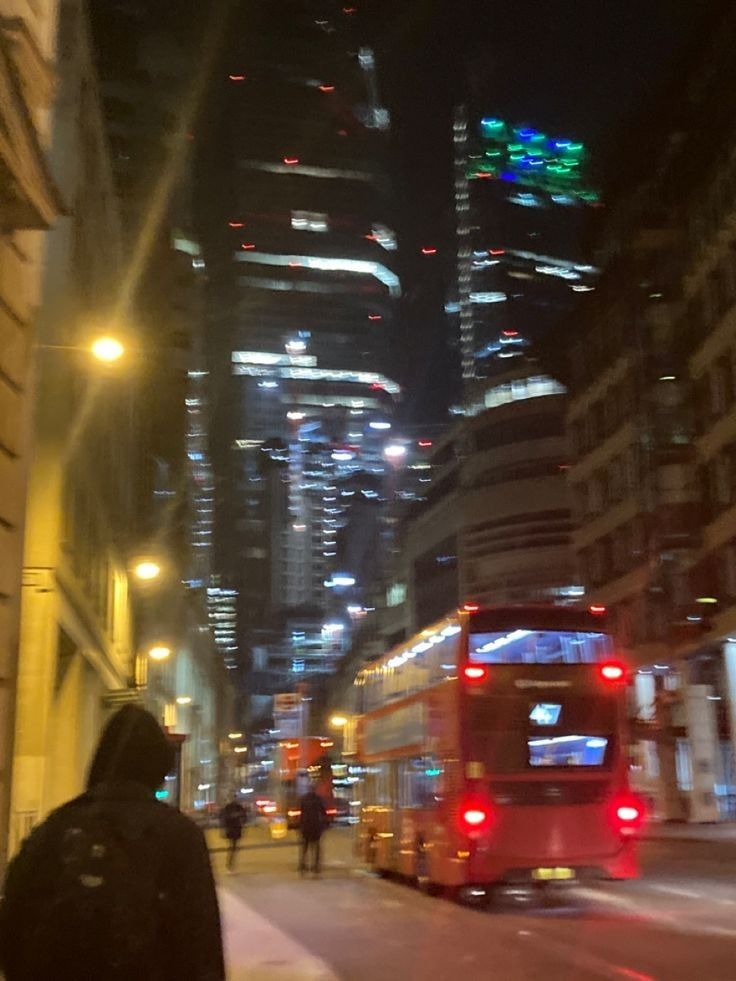 a city street at night with people walking on the sidewalk and a bus in the foreground