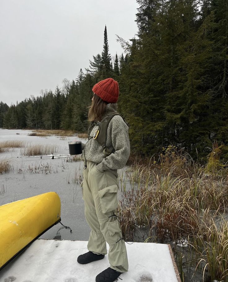 a man standing on top of a snow covered ground next to a yellow boat and trees