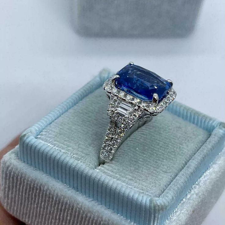 an engagement ring with a large blue stone surrounded by small white diamonds in a velvet box