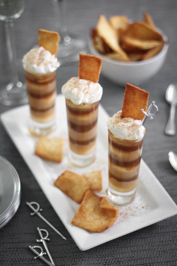 three desserts on a white plate with crackers and wine glasses in the background