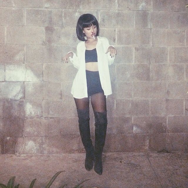 a woman standing in front of a brick wall wearing thigh high boots and a white cardigan