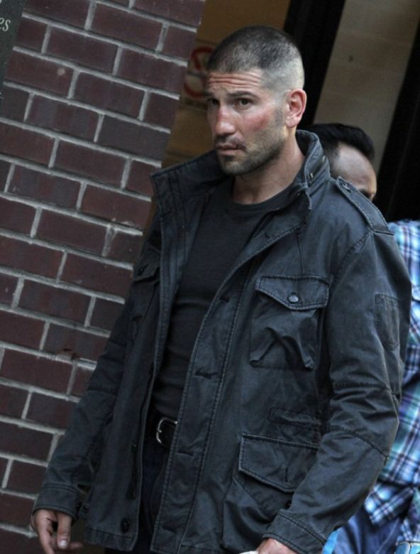 a man in black jacket holding a white frisbee next to a brick building