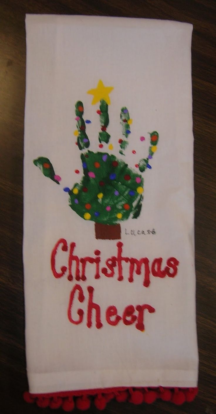 a handprinted christmas towel hanging on a table with red pom poms