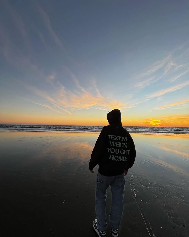 a man standing on top of a beach next to the ocean under a cloudy sky