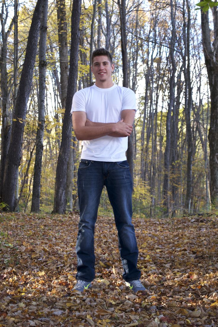 a young man standing in the woods with his arms crossed and looking at the camera