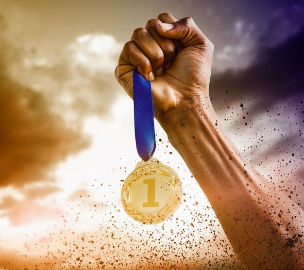 a hand holding up a gold medal with the number one on it in front of a cloudy sky