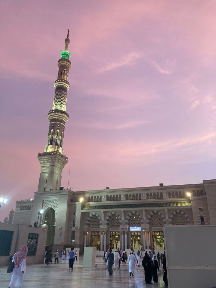 people are walking around in front of a large building with a green light on top