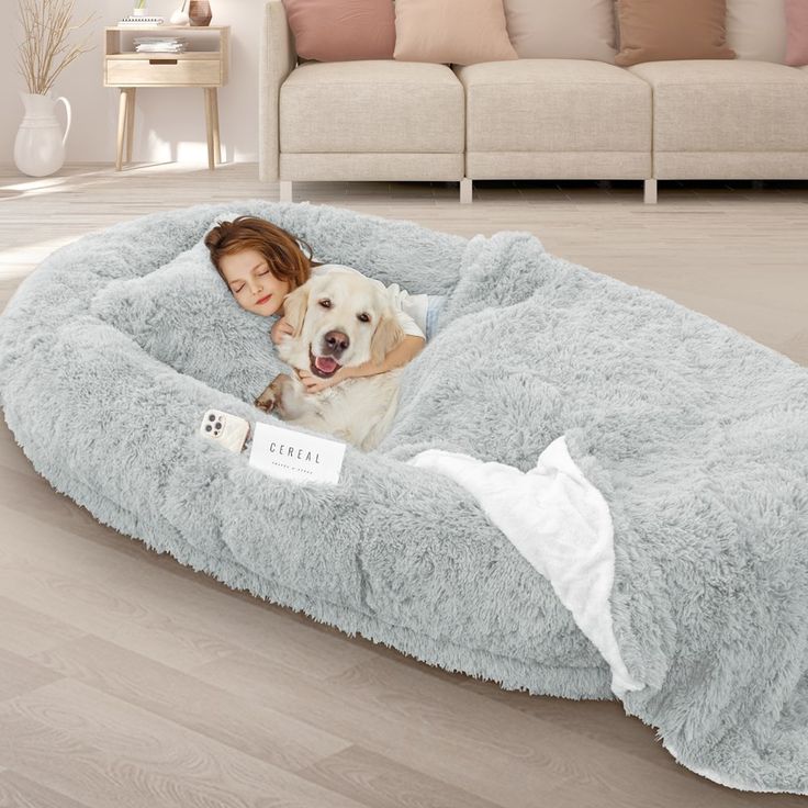 a woman laying on top of a dog bed next to a white dog in it