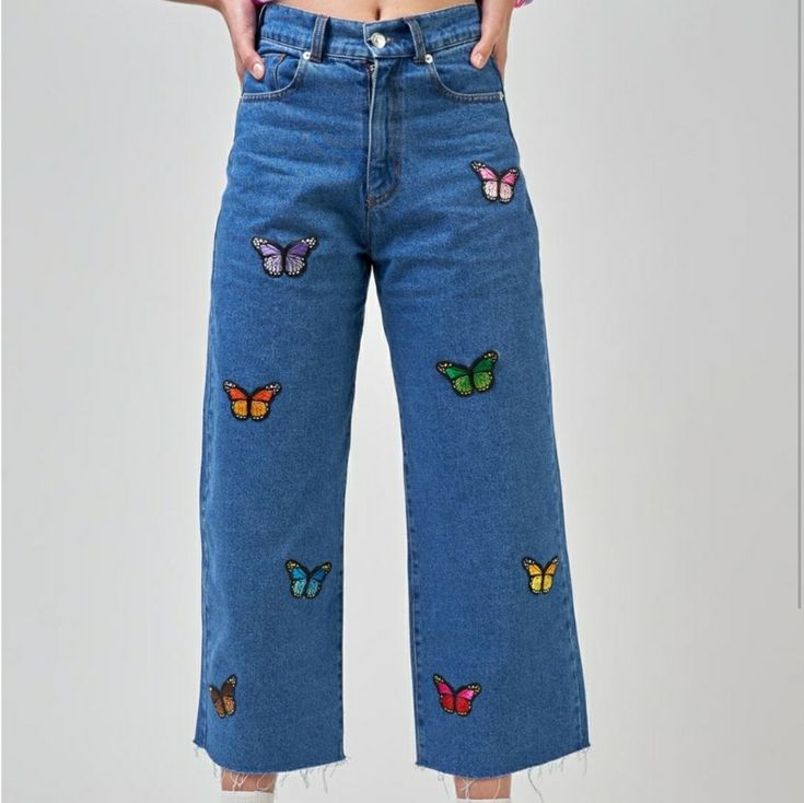 a woman wearing blue jeans with butterfly patches on the side and bottom of her pants