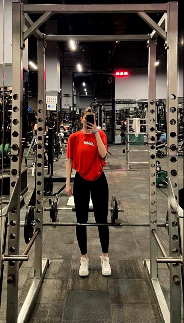 a woman taking a selfie in the gym with her cell phone to her ear