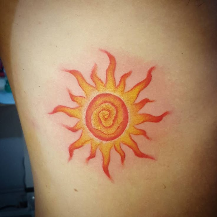 a sun tattoo on the back of a woman's upper arm, with red and yellow flames