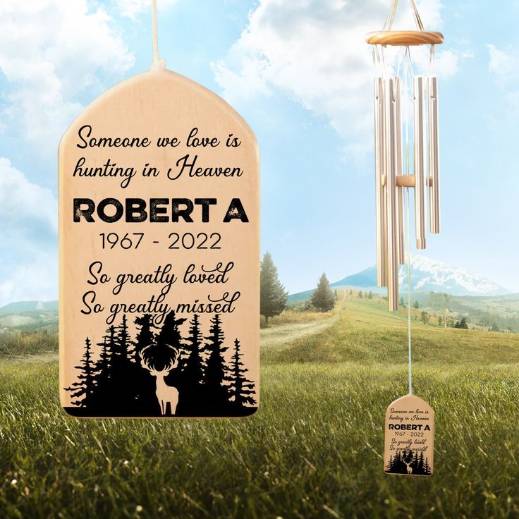 a personalized memorial wind chime in the grass with trees and mountains behind it