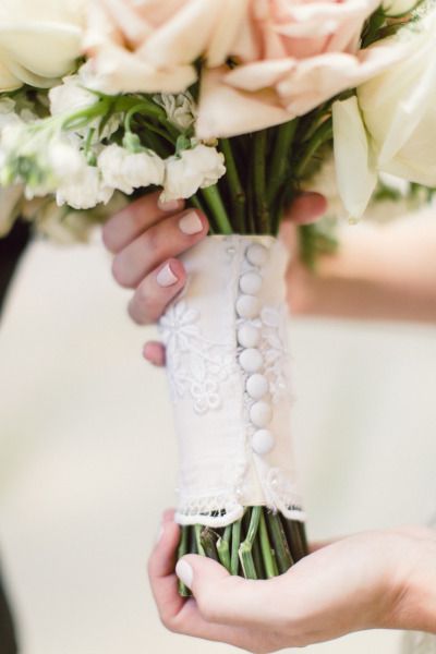 two hands holding a bouquet of white roses and other flowers in a vase with lace on it