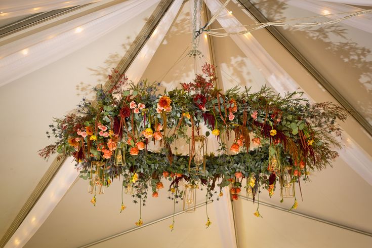 a chandelier with flowers hanging from it's sides in a white tent