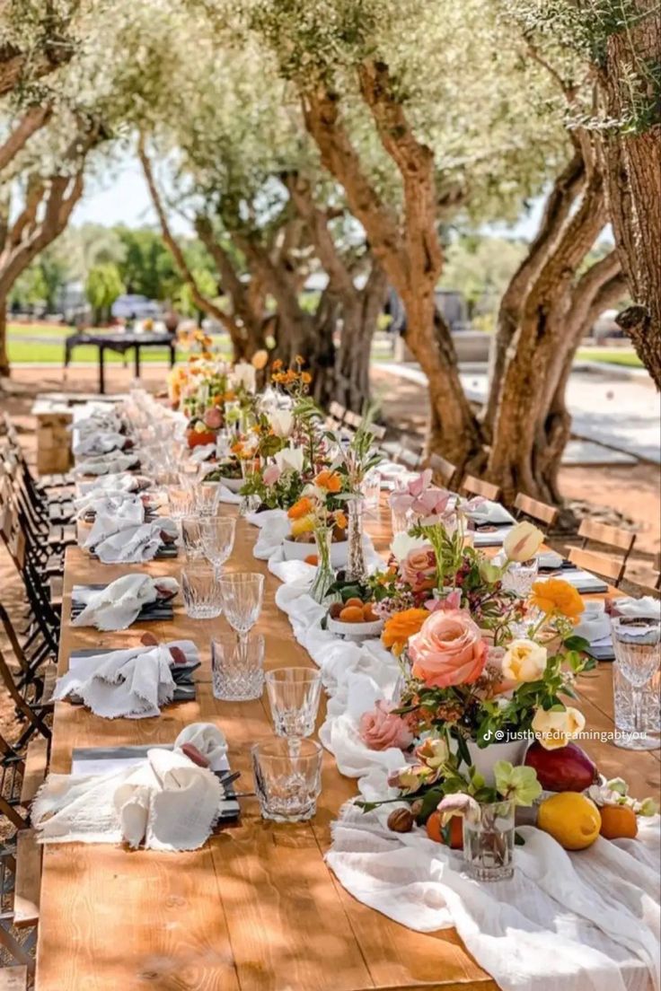 a long wooden table topped with lots of plates and glasses filled with flowers on top of it