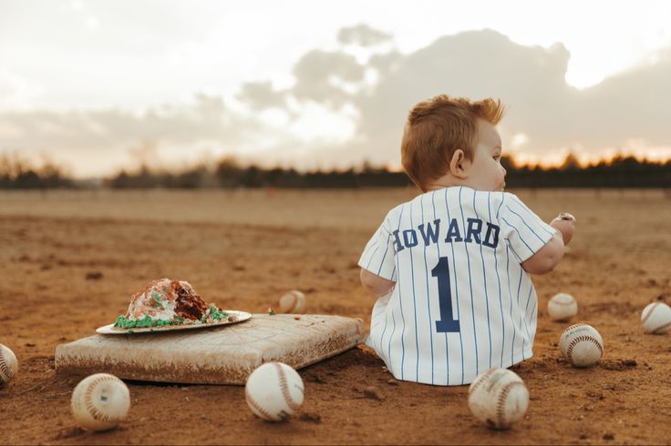 a young boy sitting on top of a baseball field next to a plate of cake