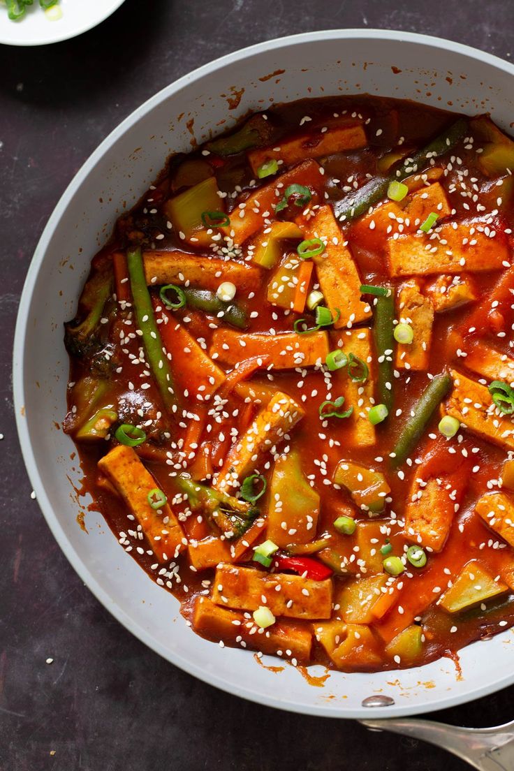 a pan filled with vegetables covered in sesame seeds and seasoning on top of a table