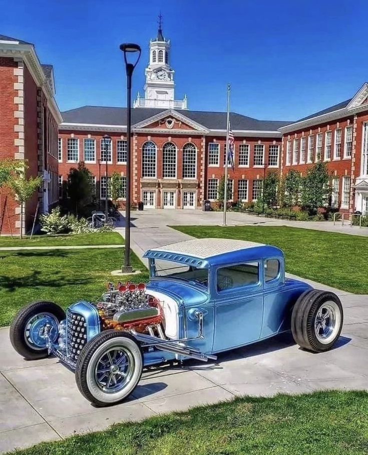 an old model t car parked in front of a brick building with a clock tower