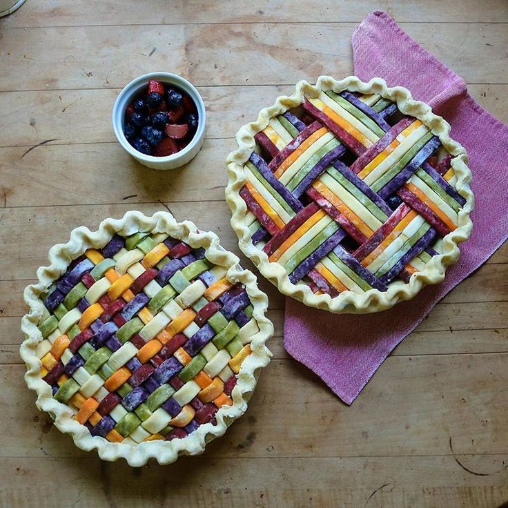 two pies sitting on top of a wooden table next to a bowl of fruit