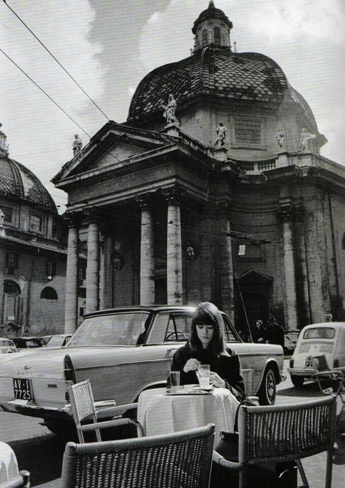 a woman sitting at an outdoor table in front of a building with columns on it