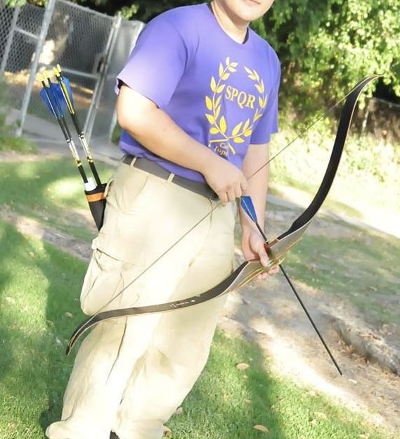 a young boy holding a bow and arrow in his hands while standing on the grass