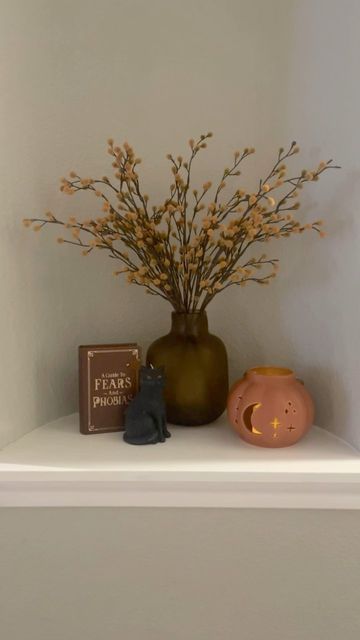 there is a vase with some flowers on the shelf next to a book and a cat figurine