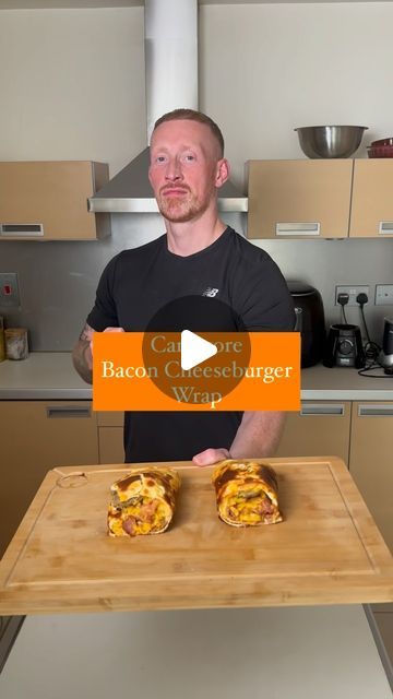 a man standing in front of a wooden cutting board with two sandwiches on top of it