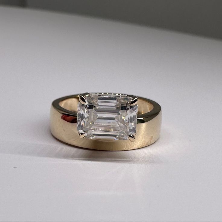 a ring with an emerald cut diamond in it sitting on a table next to a white surface