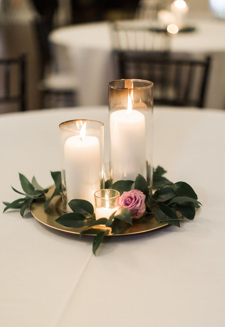 three candles are sitting on top of a plate with greenery and roses in it