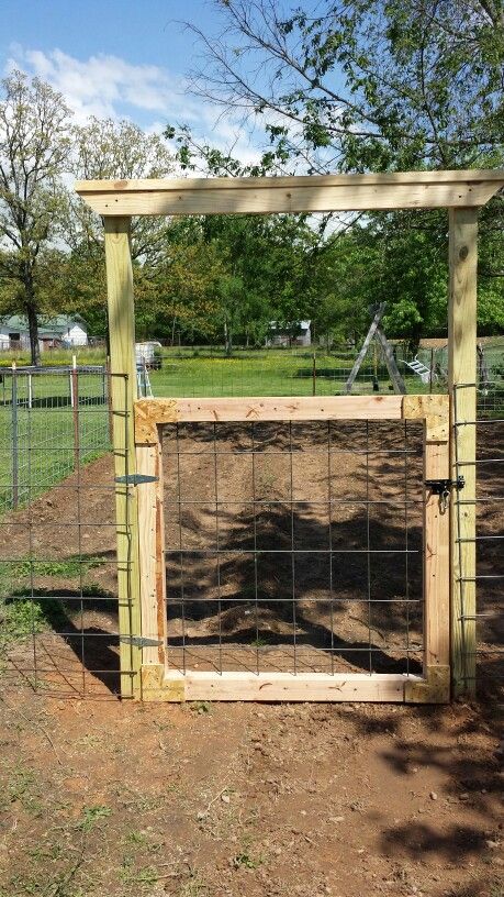 a wooden gate in the middle of a dirt field with trees and grass behind it