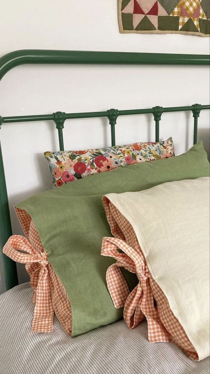 a green metal headboard with two pillows on it and an old quilt hanging above the bed