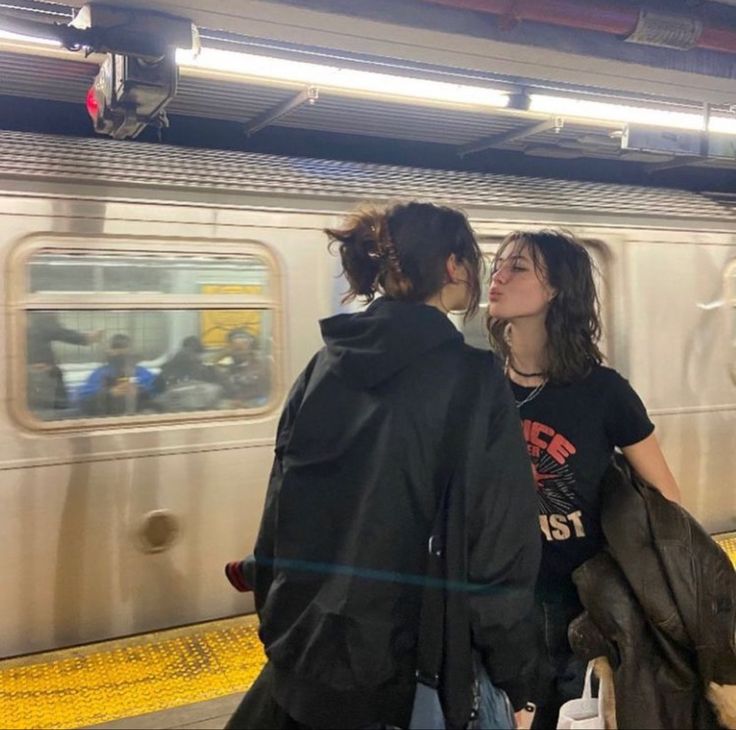 two people standing in front of a subway train at the station, one is kissing the other's forehead