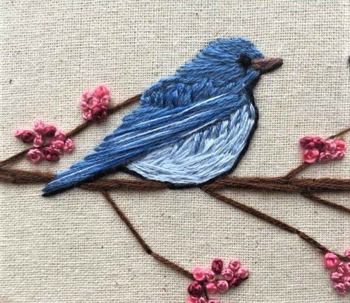 a blue bird sitting on top of a branch with pink flowers in it's beak