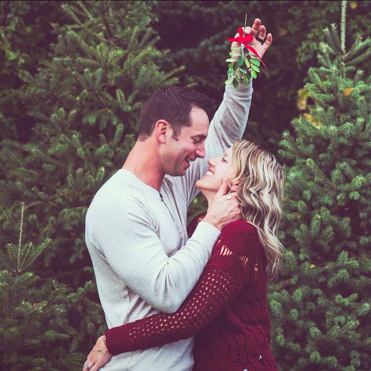 a man and woman standing next to each other in front of christmas trees with their arms around each other