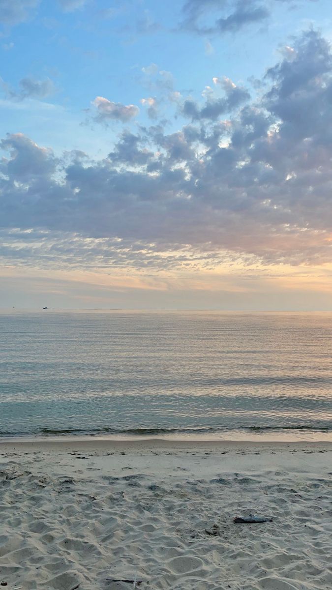 two people walking on the beach carrying surfboards under a cloudy blue sky at sunset