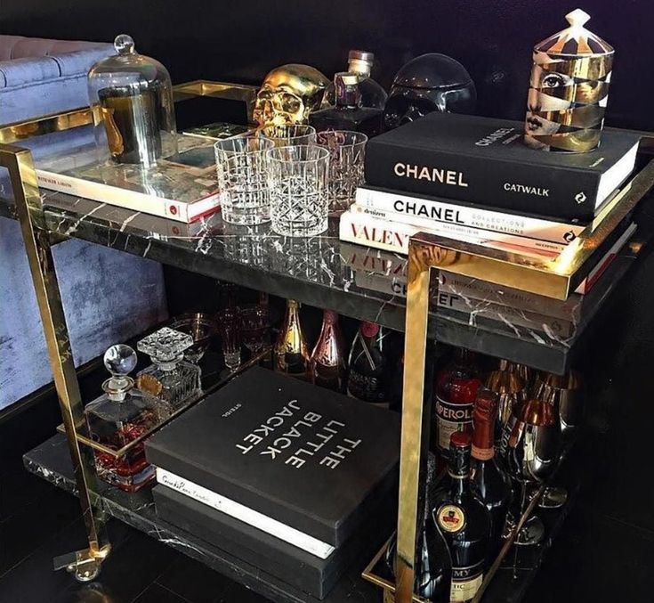 a black and gold bar cart with books, glasses, liquor bottles and other items