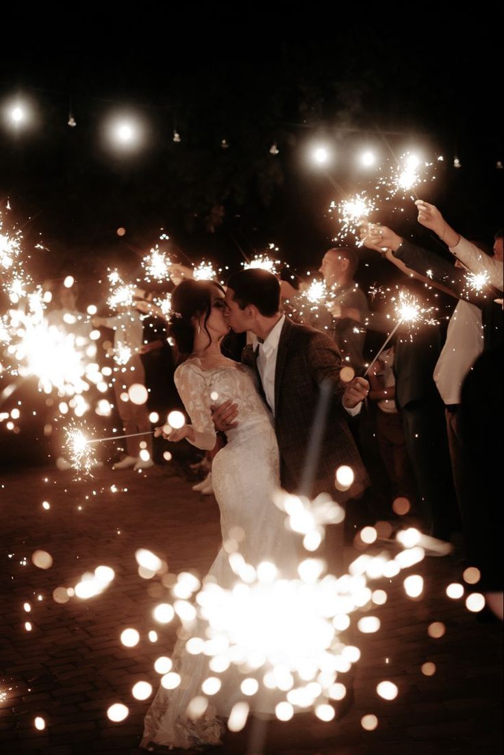 a bride and groom kiss as they hold sparklers in their hands while surrounded by confetti